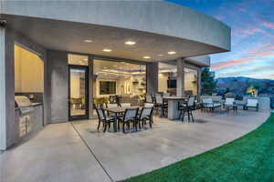 Patio terrace at dusk featuring a grill, a mountain view, exterior bar, and exterior kitchen