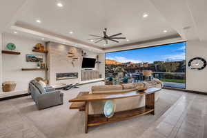 Living room with a large fireplace, a raised ceiling, and ceiling fan