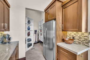 Kitchen with light stone counters, stainless steel fridge, and decorative backsplash