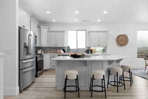 Kitchen with light hardwood / wood-style flooring, appliances with stainless steel finishes, white cabinetry, a kitchen breakfast bar, and a kitchen island