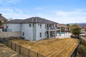 Rear view of property featuring a fenced in pool, a lawn, a patio area, and a balcony