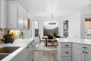 Kitchen featuring sink, hanging light fixtures, white cabinets, decorative backsplash, and light wood-type flooring