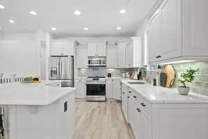 Kitchen with sink, a breakfast bar area, white cabinetry, stainless steel appliances, and a kitchen island