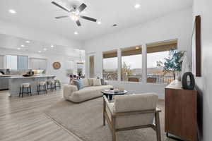 Living room with ceiling fan with notable chandelier and light hardwood / wood-style floors