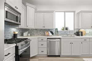 Kitchen featuring sink, white cabinets, stainless steel appliances, light stone countertops, and backsplash