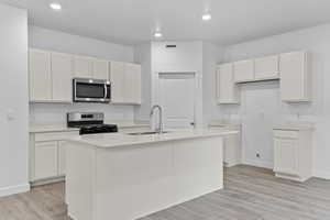 Kitchen with sink, light wood-type flooring, appliances with stainless steel finishes, a kitchen island with sink, and white cabinets