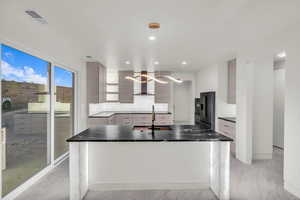 Kitchen with wall chimney exhaust hood, sink, hanging light fixtures, high end black fridge, and backsplash