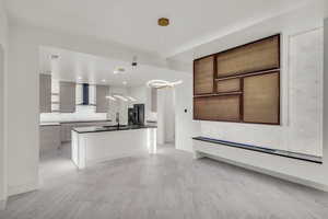 Kitchen with pendant lighting, tasteful backsplash, an island with sink, sink, and wall chimney range hood