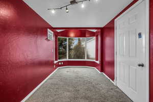 Carpeted empty room featuring rail lighting and lofted ceiling