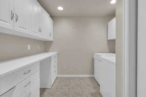 Clothes washing area with separate washer and dryer, light tile patterned floors, and cabinets