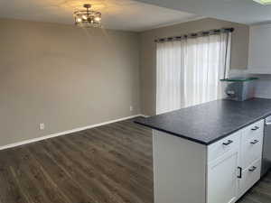 Kitchen with dishwasher, white cabinetry, an inviting chandelier, dark hardwood / wood-style flooring, and decorative backsplash