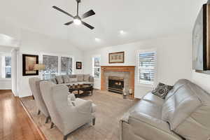 Living room with ceiling fan, a fireplace, vaulted ceiling, and light hardwood / wood-style flooring