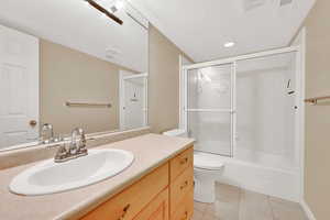 Full bathroom with tile patterned floors, toilet, bath / shower combo with glass door, a textured ceiling, and vanity