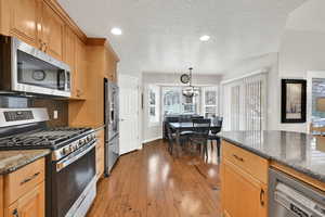 Kitchen featuring hardwood / wood-style floors, decorative light fixtures, dark stone countertops, backsplash, and stainless steel appliances