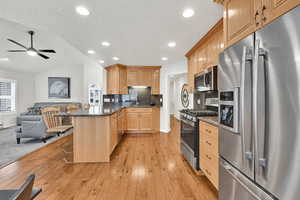 Kitchen with a breakfast bar area, stainless steel appliances, light brown cabinetry, decorative backsplash, and dark stone counters