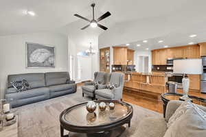 Living room featuring vaulted ceiling, sink, ceiling fan with notable chandelier, and light wood-type flooring