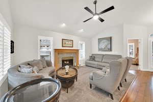 Living room with ceiling fan, lofted ceiling, a fireplace, and light hardwood / wood-style floors