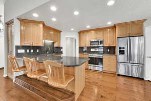 Kitchen featuring dark stone countertops, stainless steel appliances, kitchen peninsula, and light wood-type flooring