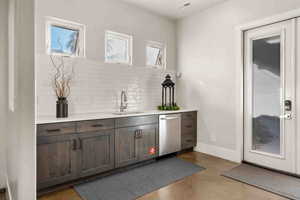 Bar with dishwasher, dark brown cabinets, sink, and decorative backsplash