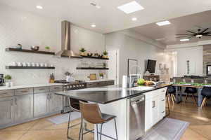 Kitchen with a kitchen bar, sink, white cabinetry, stainless steel appliances, and wall chimney range hood