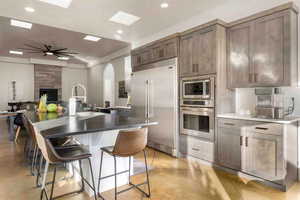 Kitchen featuring a kitchen bar, built in appliances, an island with sink, ceiling fan, and backsplash