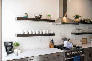 Kitchen featuring decorative backsplash, wall chimney exhaust hood, stainless steel stove, and dark brown cabinets