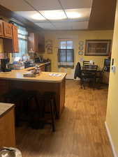 Kitchen with light hardwood / wood-style flooring, a kitchen breakfast bar, a wealth of natural light, a drop ceiling, and kitchen peninsula