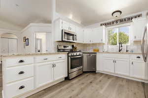 Kitchen with sink, white cabinetry, light stone counters, light wood-type flooring, and appliances with stainless steel finishes