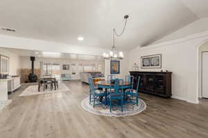 Dining area featuring lofted ceiling, a chandelier, a textured ceiling, a wood stove, and hardwood / wood-style floors