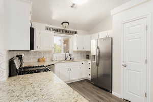 Kitchen with stainless steel appliances, white cabinetry, sink, and light stone counters