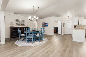 Dining room with lofted ceiling, ceiling fan with notable chandelier, and light hardwood / wood-style flooring