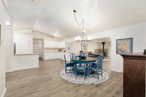 Dining room with lofted ceiling, a chandelier, light hardwood / wood-style floors, and a wood stove