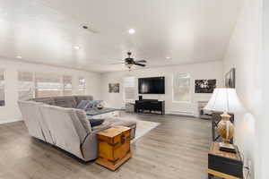 Living room featuring ceiling fan, a baseboard heating unit, a textured ceiling, and light wood-type flooring