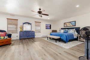 Bedroom featuring a baseboard heating unit, a textured ceiling, light hardwood / wood-style floors, and ceiling fan