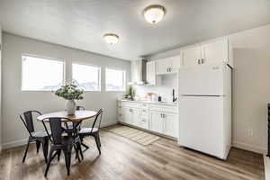 Kitchen featuring white cabinetry, sink, white refrigerator, a textured ceiling, and light hardwood / wood-style flooring