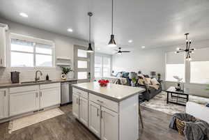 Kitchen featuring sink, stainless steel dishwasher, white cabinets, and decorative light fixtures