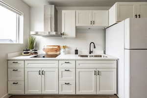 Kitchen featuring sink, white cabinetry, white refrigerator, black electric stovetop, and wall chimney exhaust hood