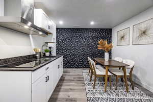 Kitchen with black electric cooktop, white cabinets, sink, and wall chimney range hood