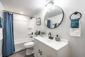 Full bathroom with hardwood / wood-style floors, vanity, a textured ceiling, toilet, and shower / bath combo with shower curtain