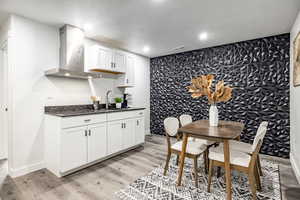 Kitchen with white cabinetry, sink, wall chimney range hood, a textured ceiling, and light hardwood / wood-style flooring