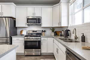 Kitchen with sink, white cabinetry, tasteful backsplash, stainless steel appliances, and light stone countertops