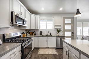 Kitchen featuring appliances with stainless steel finishes, white cabinetry, sink, hanging light fixtures, and dark wood-type flooring