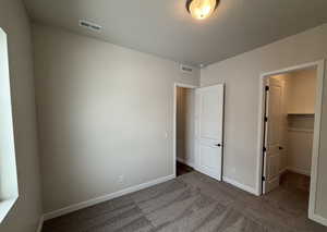 Unfurnished bedroom with a walk in closet, dark carpet, and a textured ceiling