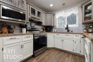 Kitchen with light hardwood / wood-style flooring, pendant lighting, stainless steel appliances, light stone countertops, and backsplash