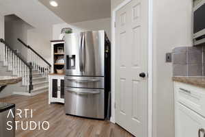 Kitchen with white cabinetry, beverage cooler, stainless steel fridge, and light hardwood / wood-style flooring