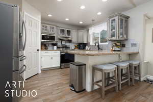 Kitchen featuring hanging light fixtures, light wood-type flooring, kitchen peninsula, stainless steel appliances, and decorative backsplash