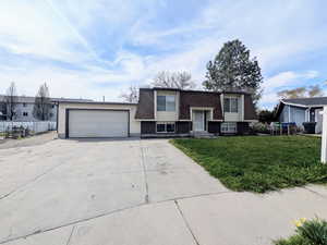 Bi-level home with a front lawn, fence, a garage, and concrete driveway