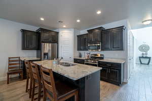 Kitchen with sink, light wood-type flooring, stainless steel appliances, light stone countertops, and a kitchen island with sink