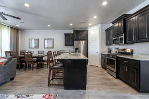 Kitchen with light wood-type flooring, a kitchen breakfast bar, stainless steel appliances, light stone countertops, and a kitchen island with sink