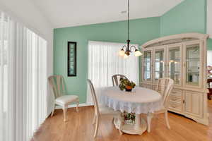 Dining area with a notable chandelier, vaulted ceiling, and light wood-type flooring